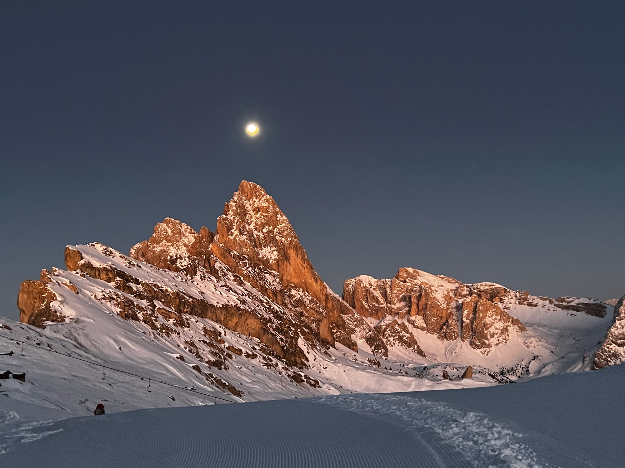 Pista appena battuta all'alba sotto le cime delle Dolomiti, con la luna
